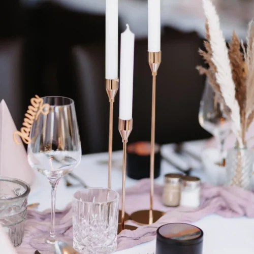 festlich gedeckter Tisch mit Hochzeitsdeko. Goldene Kerzenständer, goldenes Besteck mit Trockenblumen und Tischläufer in rosa